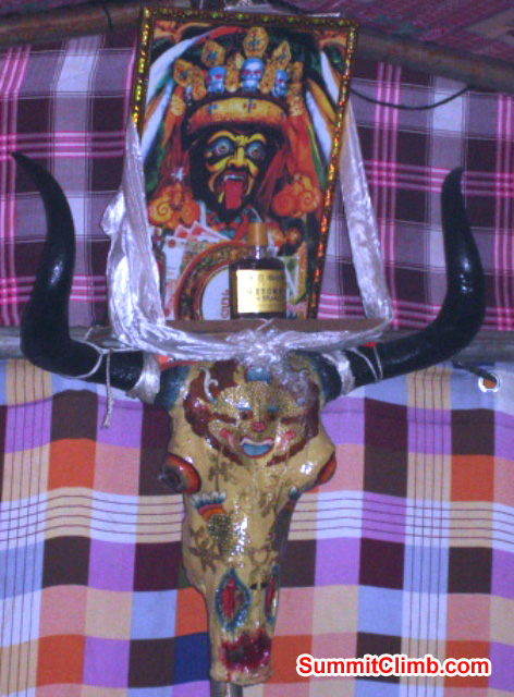 A scary painting, a bottle of spirit, and an adorned yak skull watch over a teahouse tent in basecamp. Photo by James Grieve